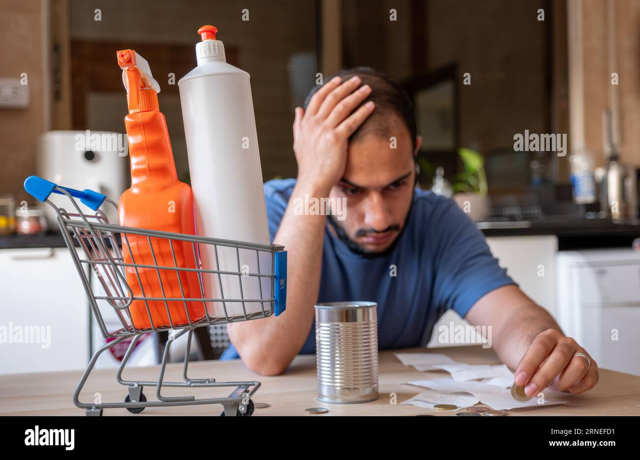 l'uomo seduto in cucina si sentiva frustrato a causa dell'inflazione e dell'aumento delle necessità quotidiane di provviste per la casa con il carrello davanti a sé Foto Stock