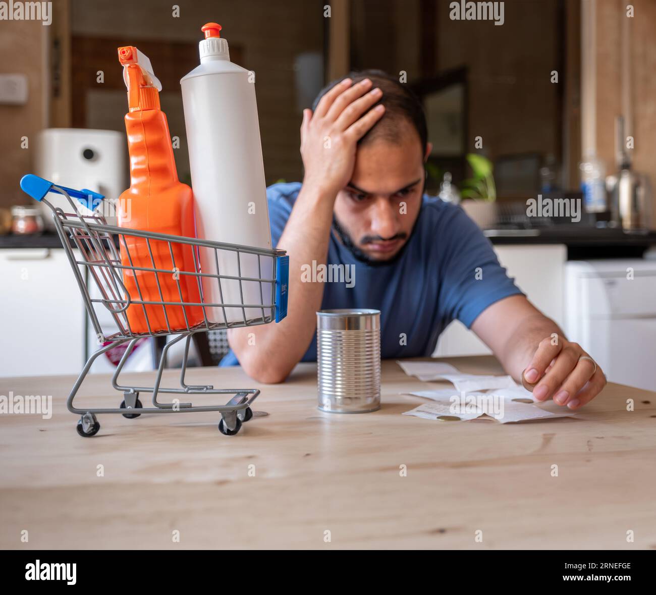 l'uomo seduto in cucina si sentiva frustrato a causa dell'inflazione e dell'aumento delle necessità quotidiane di provviste per la casa con il carrello davanti a sé Foto Stock