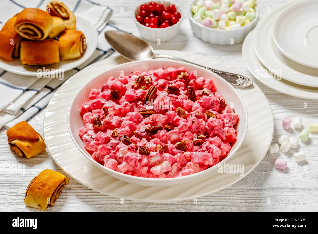 Insalata cremosa di mirtilli rossi con mini marshmallow, mela fresca e noci pecan in ciotola bianca su tavolo di legno bianco con dolci alla cannella, Natale americano Foto Stock