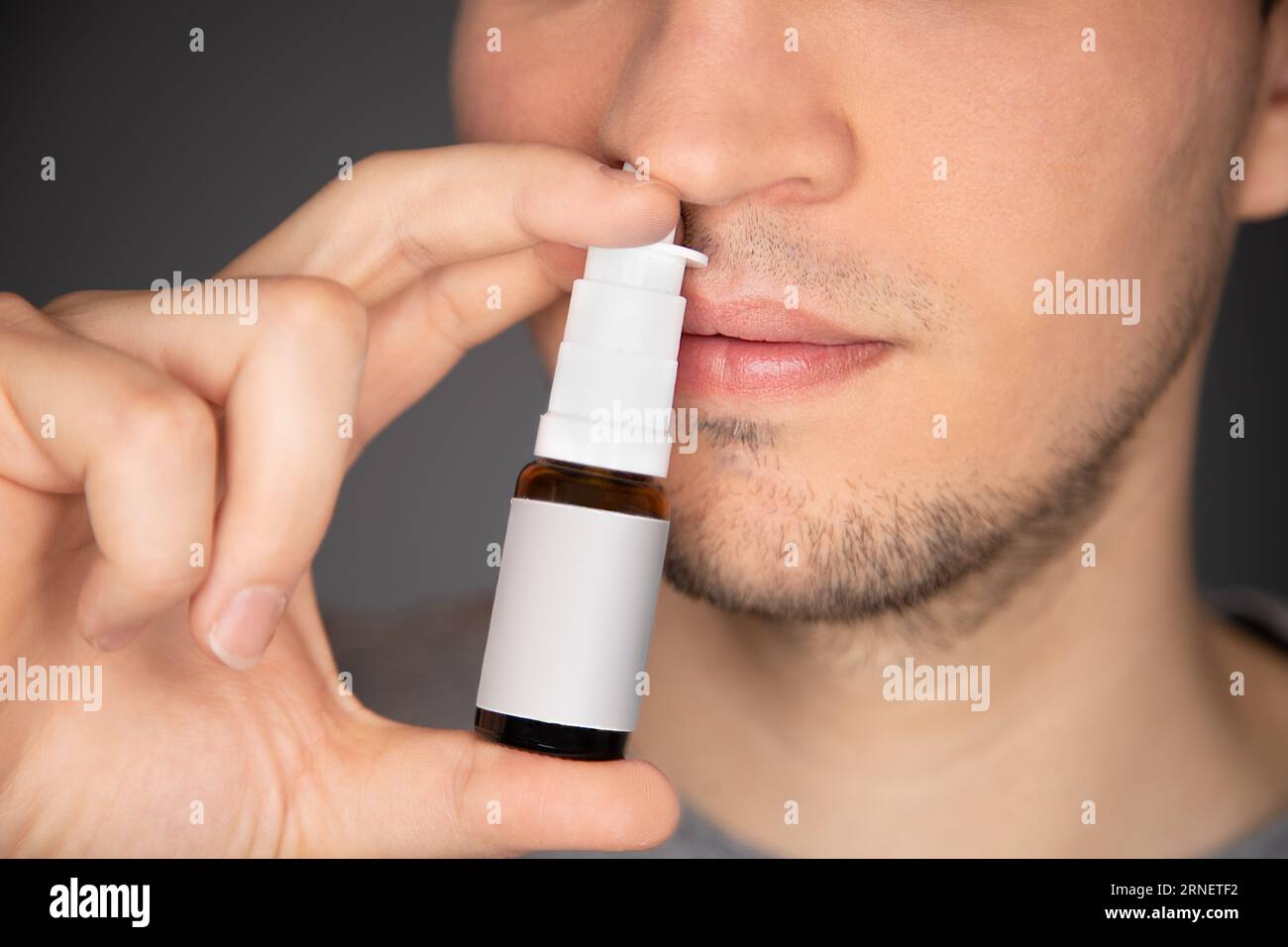 il giovane usa spray nasale e applica il flacone al naso mentre pompa la medicina al setto per alleviare la congestione, prurito e naso che cola e snee Foto Stock