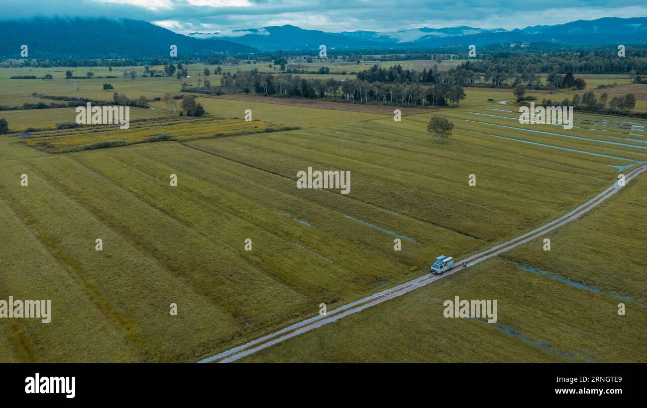 Vasti campi nella regione centrale della slovenia dopo le pesanti inondazioni dell'estate del 2023, con un furgone visibile parcheggiato su una strada di ghiaia. Vanlife nel vecchio furgone in Foto Stock