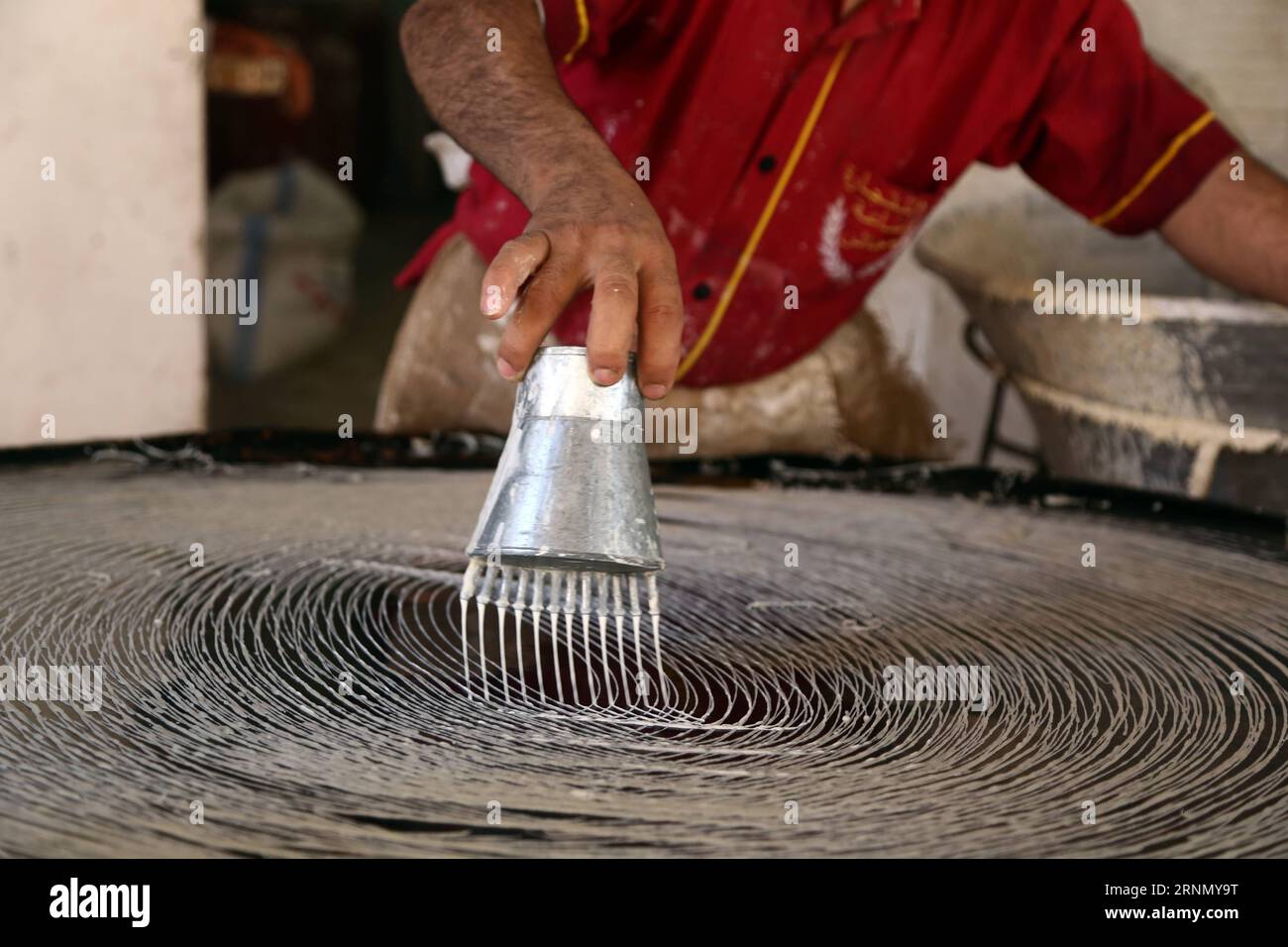 (170616) -- GIZA, 16 giugno 2017 -- un panettiere egiziano produce kunafa, un dolce tradizionale egiziano, versando circolarmente l'impasto liquefatto attraverso un filtro a forma di tazza sulla superficie del forno all'esterno di un grande negozio di pasticceria nel distretto di Faysal, nella provincia egiziana di Giza, 15 giugno 2017. Sopravvissuti nel corso dei secoli, il kunafa e il qatayef sono costituiti da una miscela di farina, acqua, latte in polvere e altri materiali. I clienti di diverse età, tra cui uomini, donne e bambini, acquistano kunafa e qatayef per cucinarli prima del tramonto, la fine della giornata di digiuno, per gustare i dessert dopo il pasto veloce Foto Stock