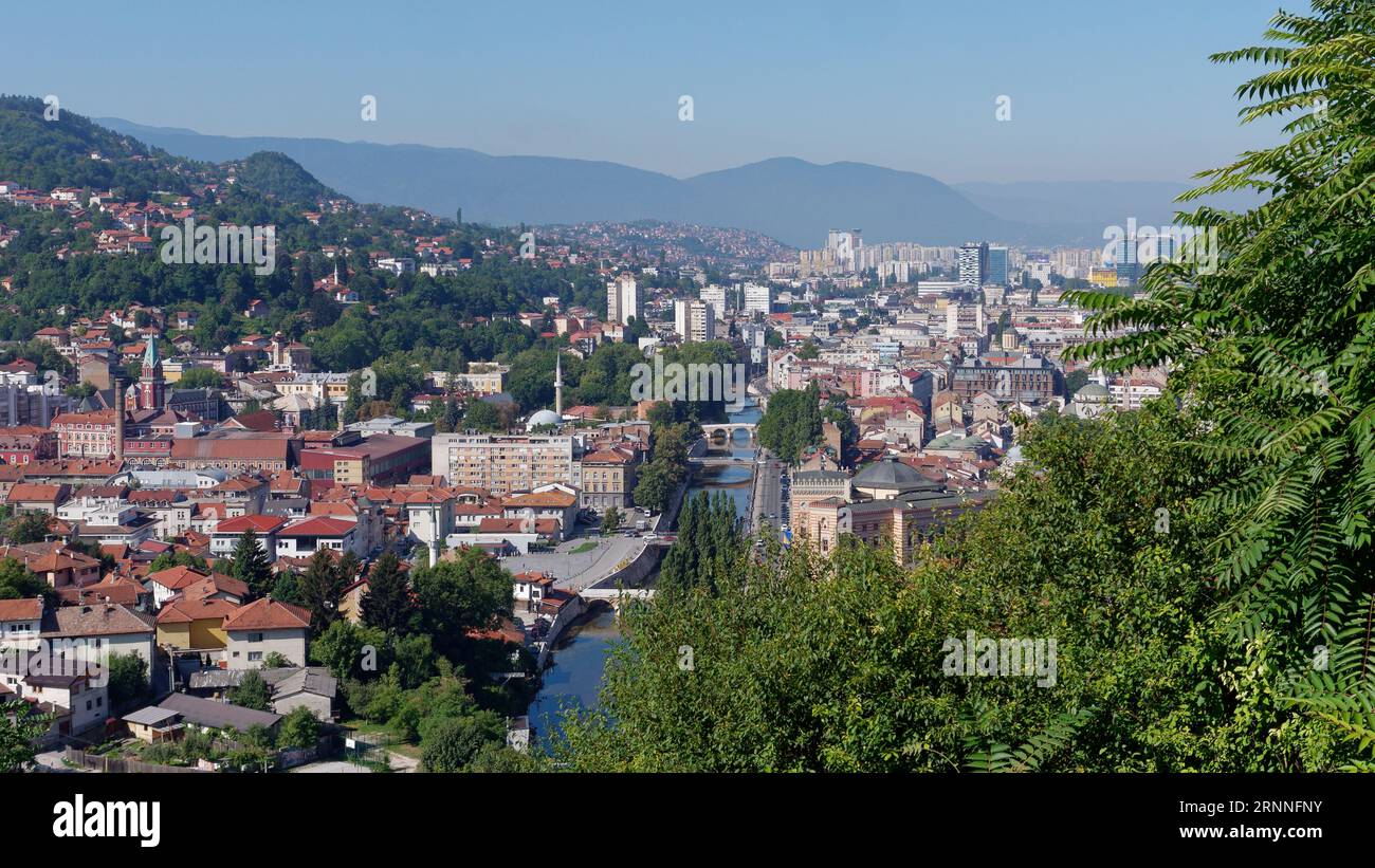 Paesaggio urbano di Sarajevo con il fiume Miljacka e la Chiesa di Sant'Antonio da Padova a sinistra e il Municipio a destra, Bosnia ed Erzegovina, 2 settembre 2023 Foto Stock