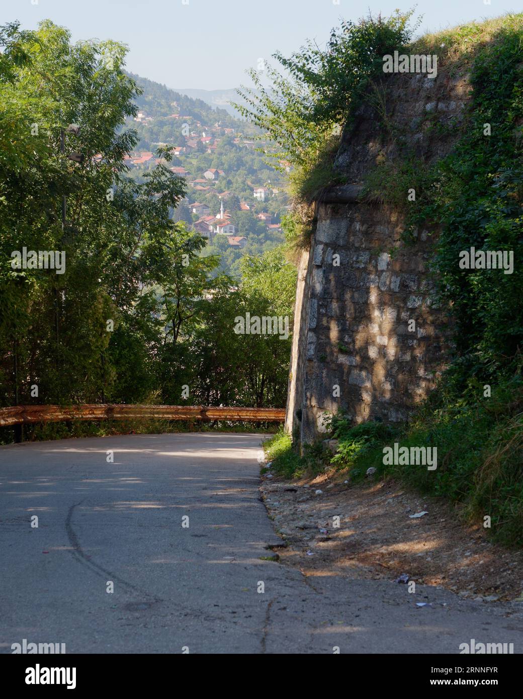 Strada sopraelevata con barriera e muro sbriciolato con vista sulle case su una montagna nella città di Sarajevo, Bosnia ed Erzegovina, 2 settembre 2023 Foto Stock