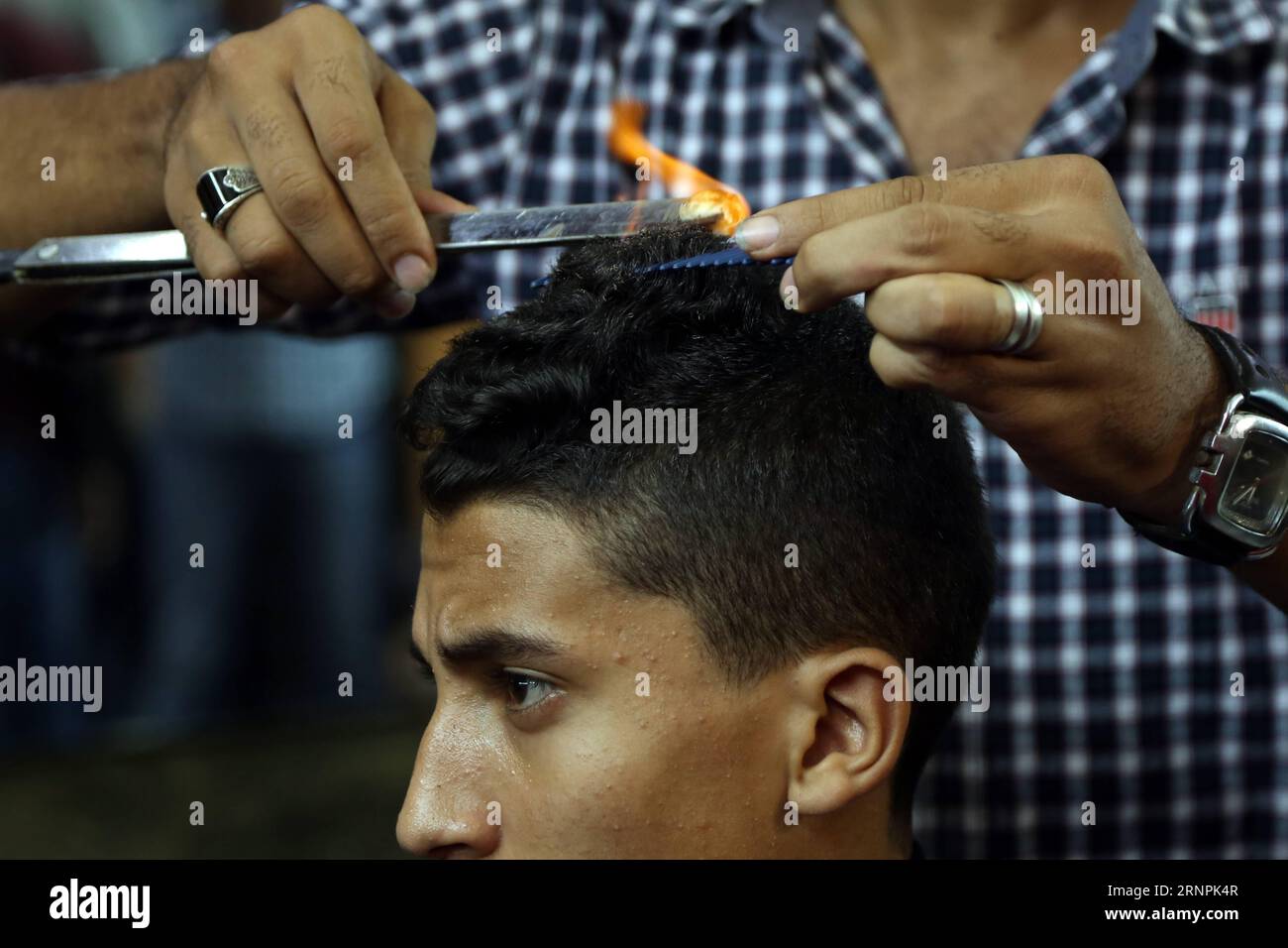 (170831) -- GIZA (EGITTO), 31 agosto 2017 -- Un barbiere acconcia i capelli di un cliente con palle di fuoco in un barbiere situato in un quartiere della provincia egiziana di Giza vicino alla capitale il Cairo il 30 agosto 2017. Vedere fiamme di fuoco sulla testa di un cliente non è una scena comune nei barbieri di tutto il mondo, ma sta diventando più familiare e interessante alla fine in un negozio di parrucchiere in un quartiere nella provincia egiziana di Giza, vicino alla capitale il Cairo. La piccola barbiera Hamada Ramadan, nel quartiere di Kafr Tohormos, è stata brulicata di clienti, soprattutto adolescenti e bambini, che sono venuti a prendere i loro capelli Foto Stock