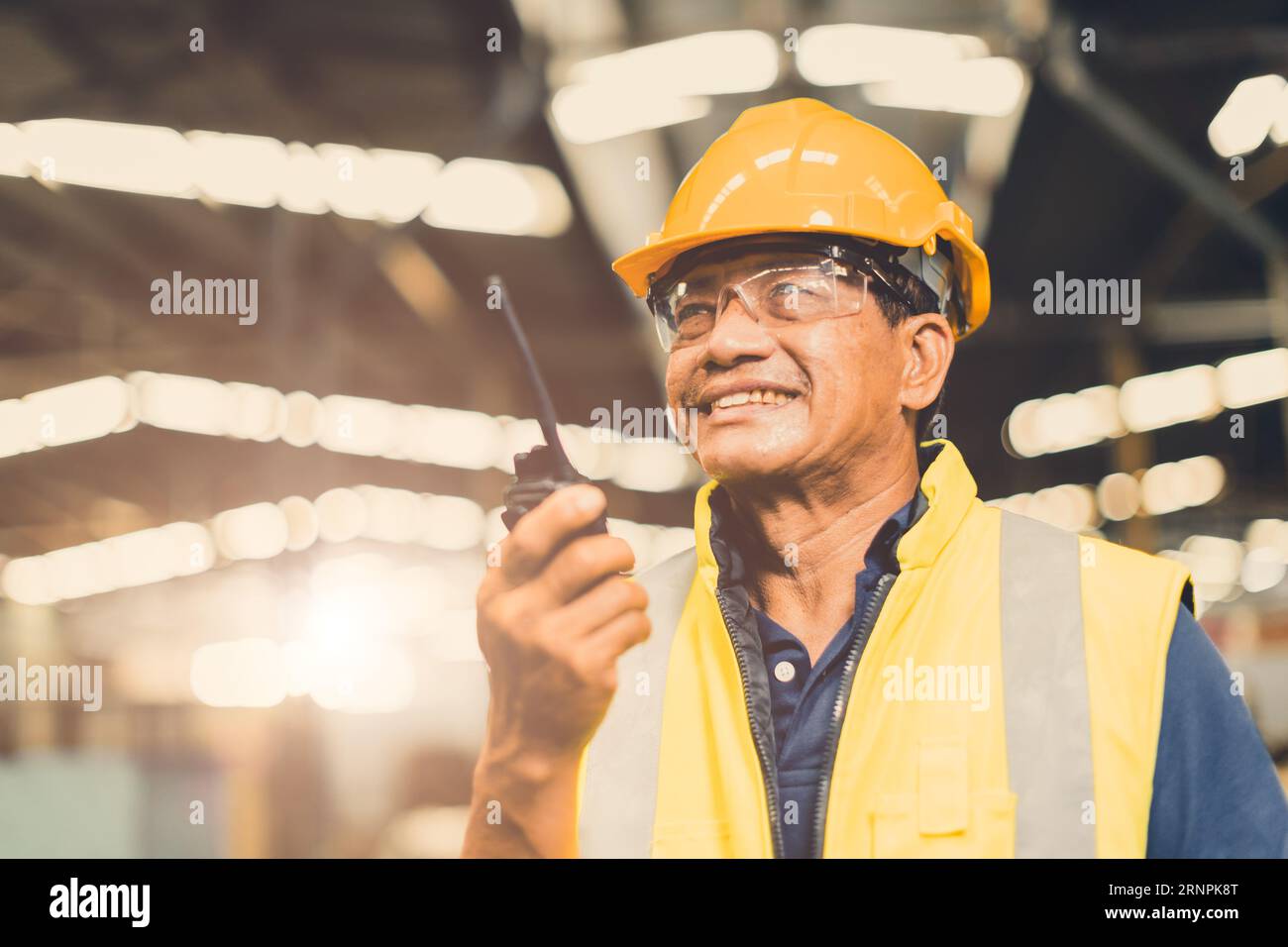 Supervisore del caposquadra adulto asiatico felice di utilizzare il radiocomando per eseguire lavori di progetto in una fabbrica industriale pesante Foto Stock