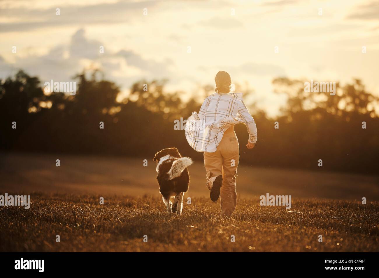 Vista posteriore di una ragazza adolescente felice mentre correva con il suo cane sul campo in un paesaggio autunnale. Gioioso proprietario di animali domestici con Czech Mountain Dog. Foto Stock
