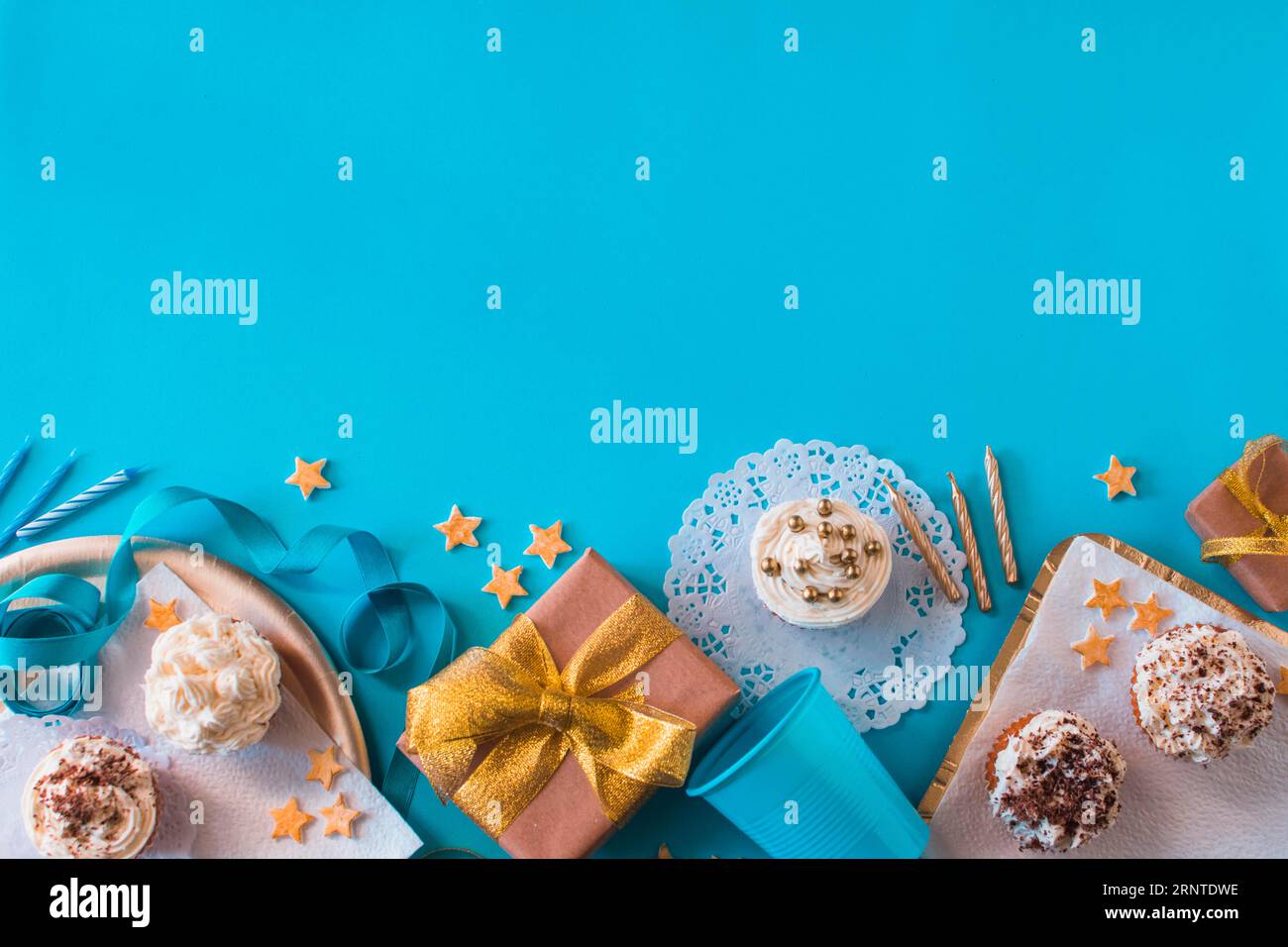 Regali di compleanno con vista rialzata e muffin candele su una superficie blu Foto Stock