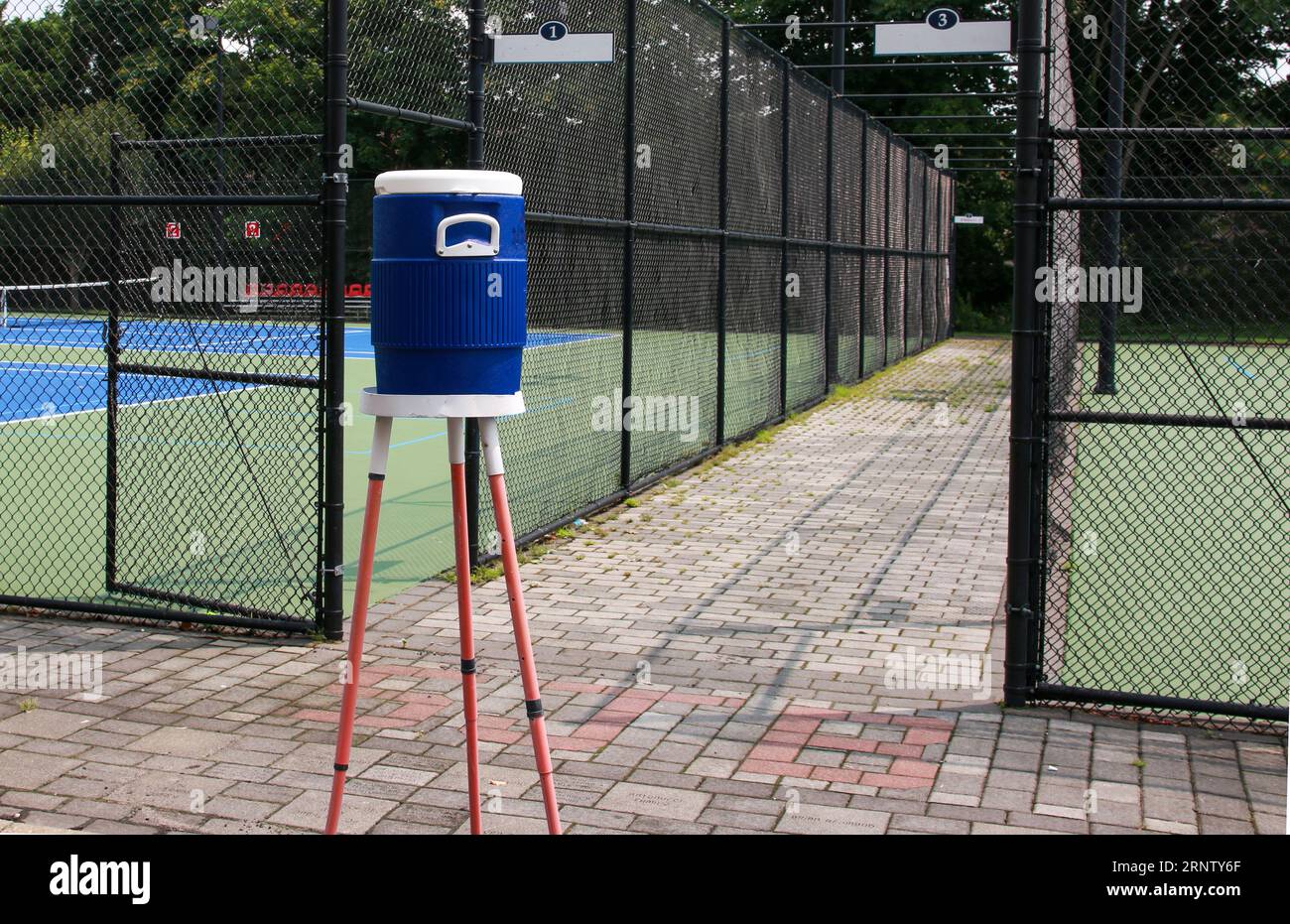 Caraffa blu su un cavalletto accanto ai campi da tennis e da picchettio circondati da recinzioni nere. Foto Stock