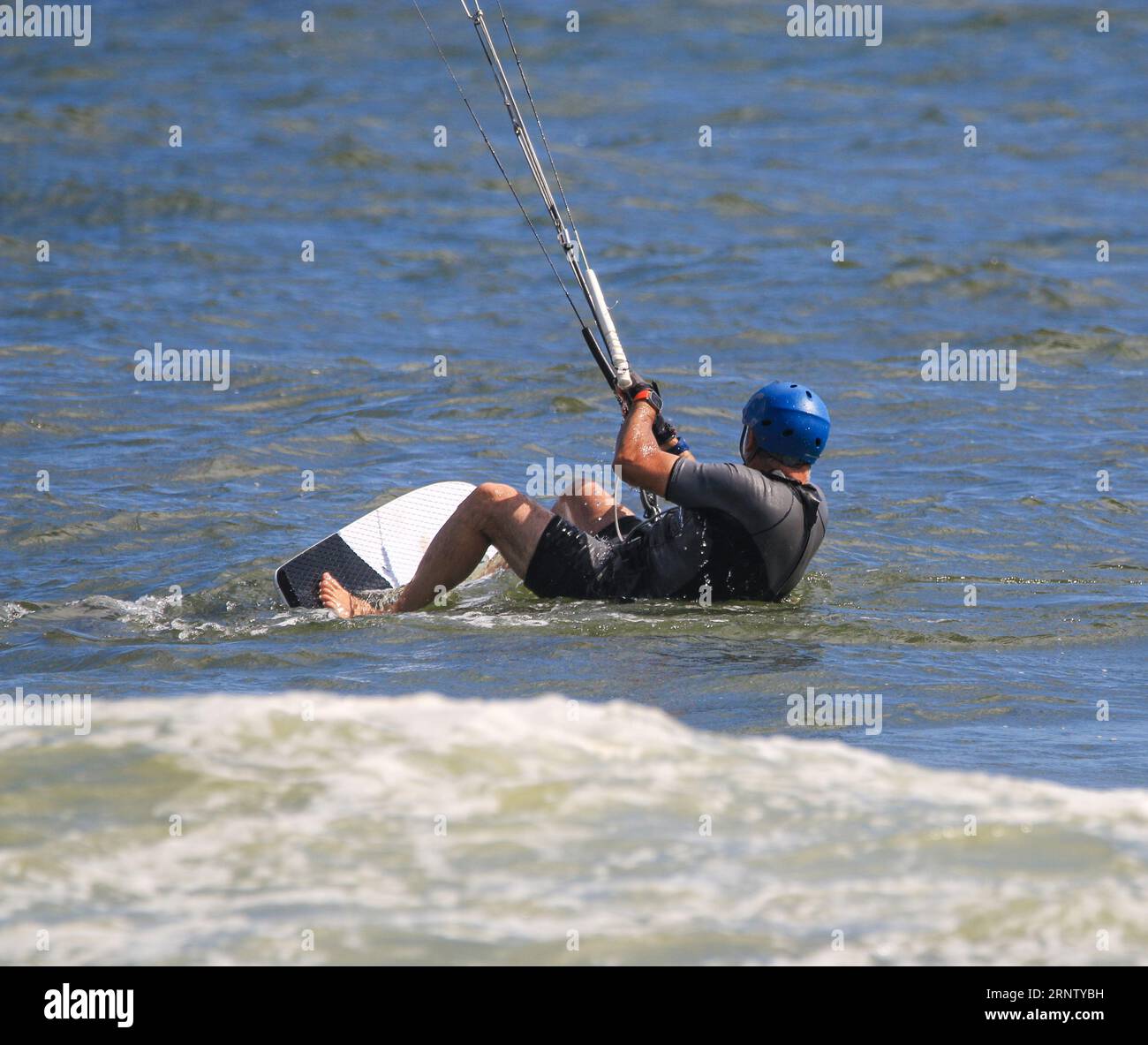 Un Kitesurfer maschio viene tirato fuori proprio all'inizio del suo giro nell'oceano indossando un casco blu. Foto Stock