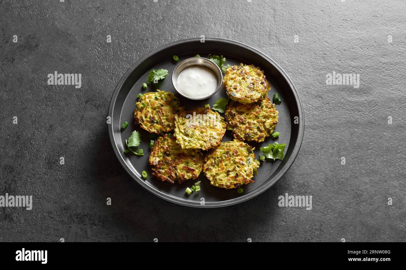 Vista ravvicinata delle frittelle vegetariane di zucchine sul piatto su fondo di pietra scura. Foto Stock
