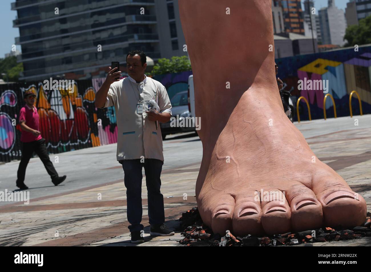 (171130) -- SAN PAOLO, 30 novembre 2017 -- Un uomo si trova di fronte a una scultura di un piede gigante che calpesta i carboni caldi, dell'artista brasiliano Eduardo Srur, a San Paolo, Brasile, il 29 novembre 2017. La scultura ha l'obiettivo di creare consapevolezza sulla polineuropatia amiloide familiare, una malattia neurologica in cui uno dei possibili sintomi è la ridotta capacità di sentire la temperatura. (Da) (fnc) (zxj) BRAZIL-SAO PAULO-HEALTH-SCULPTURE RahelxPatrasso PUBLICATIONxNOTxINxCHN Foto Stock