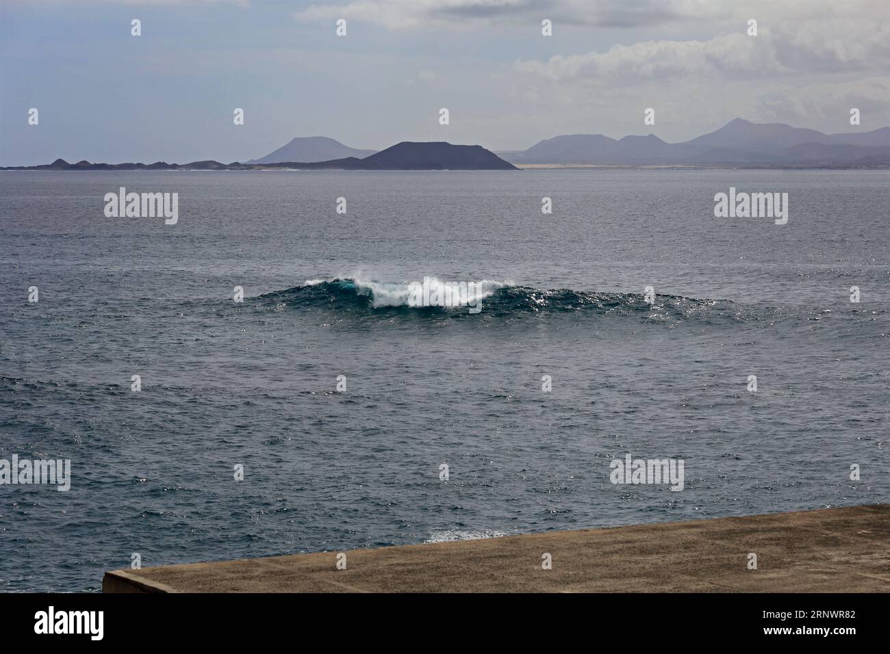 Onda singola oltre la parete del mare a Marina Rubicon, Playa Blanca, Lanzarote, Isole Canarie, Spagna - Fuerteventura in lontananza. Foto Stock