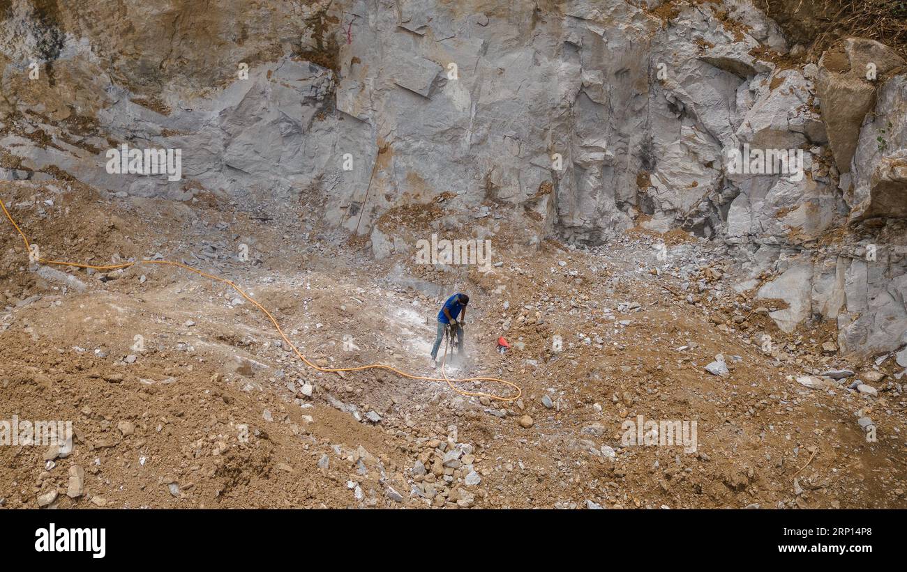Perforatrice elettrica per operai edili Drilling Mountain Ground in Construction area con sfondo roccioso Foto Stock