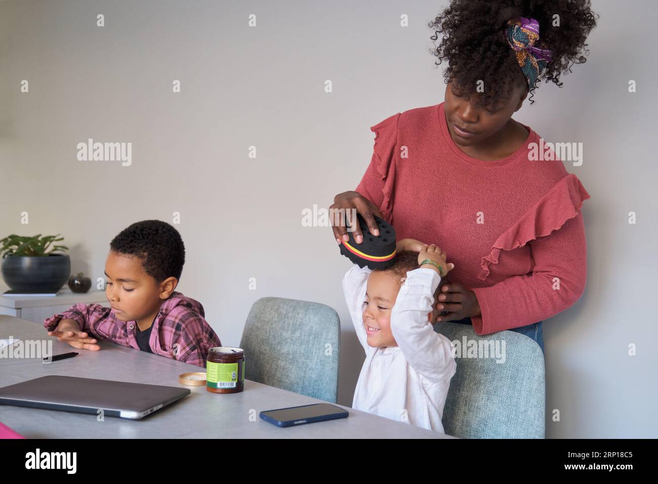 La madre africana acconcia i capelli del figlio utilizzando un'onda arricciata afro o una spugna attorcigliata. Foto Stock