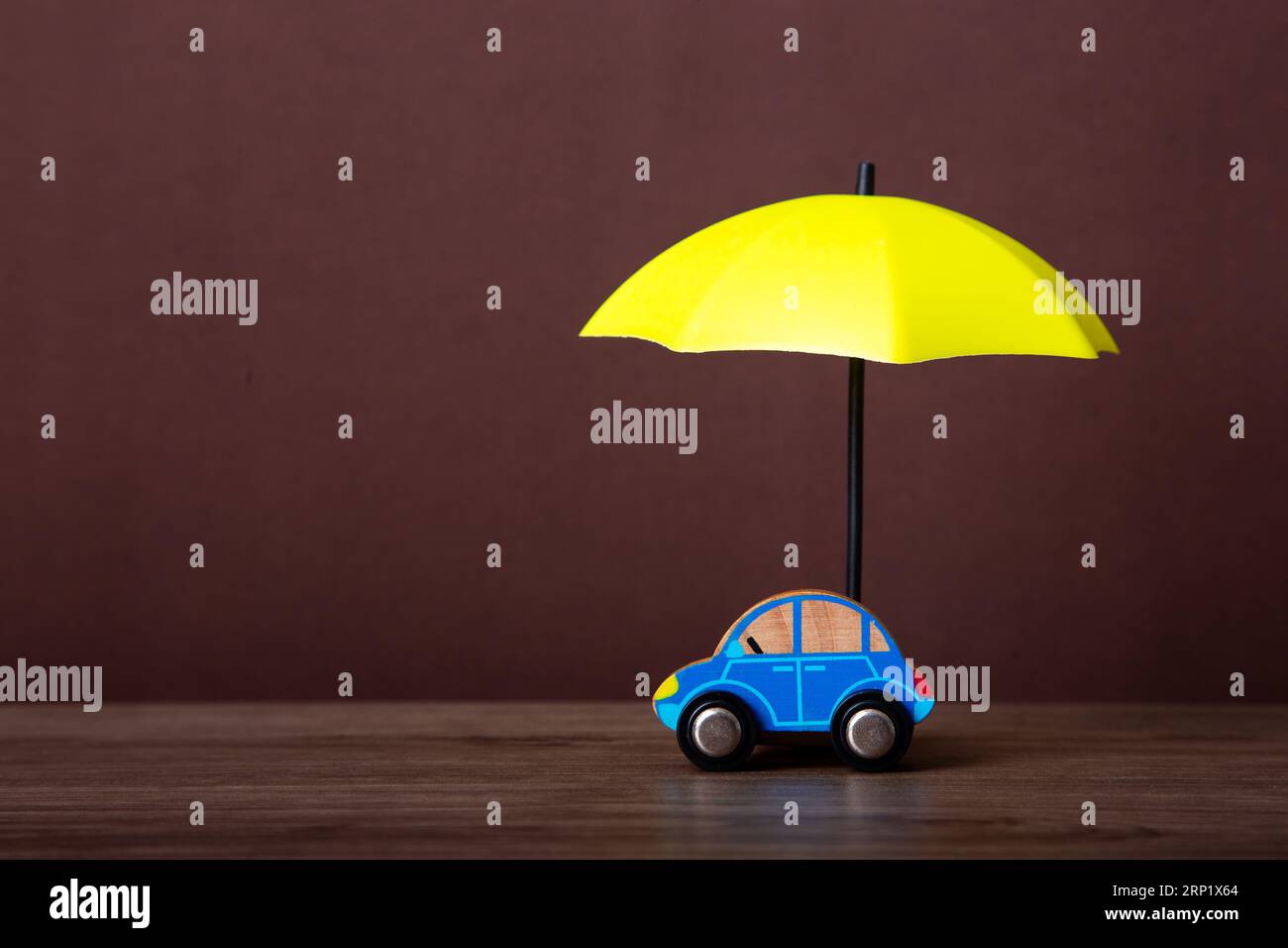 Macchina giocattolo blu protetta da un piccolo ombrello giallo su una superficie di legno. Foto Stock