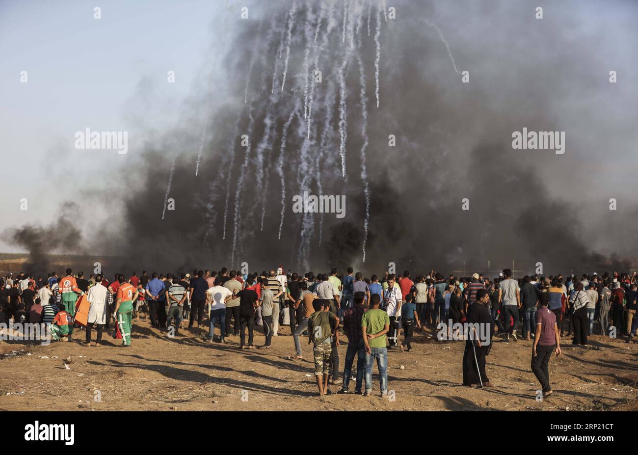 (180810) -- GAZA, 10 agosto 2018 -- i manifestanti palestinesi si riuniscono come una pioggia di bombole di gas lacrimogeni sparate dalle truppe israeliane atterrano sul campo durante gli scontri sul confine tra Gaza e Israele, a est della città di Gaza, il 10 agosto 2018. Due palestinesi, uno dei quali era medico, sono stati uccisi, e 307 palestinesi venerdì sono stati feriti in scontri vicino al confine tra Gaza e Israele, secondo il rapporto del Ministero della salute di Gaza. ) MIDEAST-GAZA-CLASH WissamxNassar PUBLICATIONxNOTxINxCHN Foto Stock