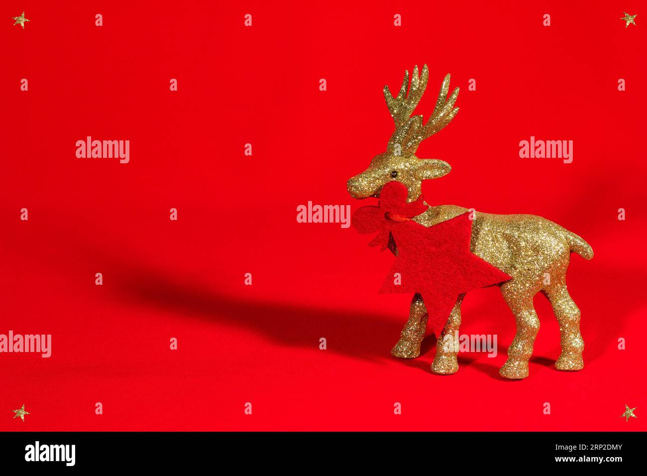 Statuetta di renne dorata e lucente su sfondo rosso. Biglietto di Natale, buono regalo, stella rossa, ciondolo. Sfondo natalizio con spazio per le copie Foto Stock