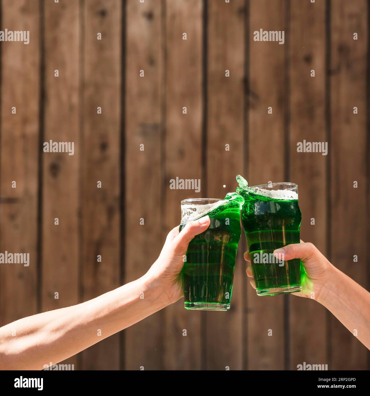 Le persone che si aggrappano agli occhiali una bevanda verde vicino a un muro di legno Foto Stock