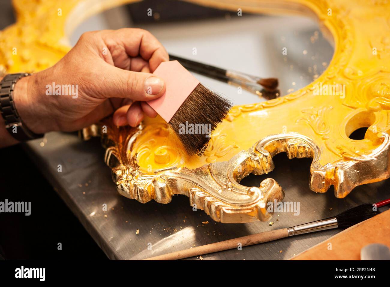 Dettaglio di uno specchio dorato con foglia d'oro, un uomo abbatte un pezzo di foglia d'oro con pinzette e lo accarezza con un pennello Foto Stock