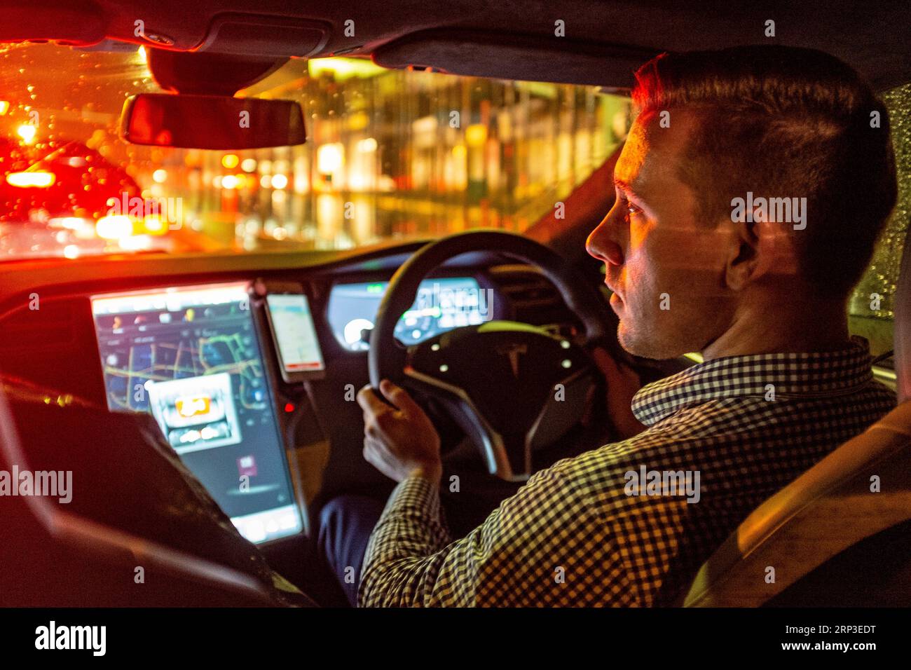 Guida Uber al volante di un veicolo elettrico Tesla di notte sotto la pioggia Foto Stock