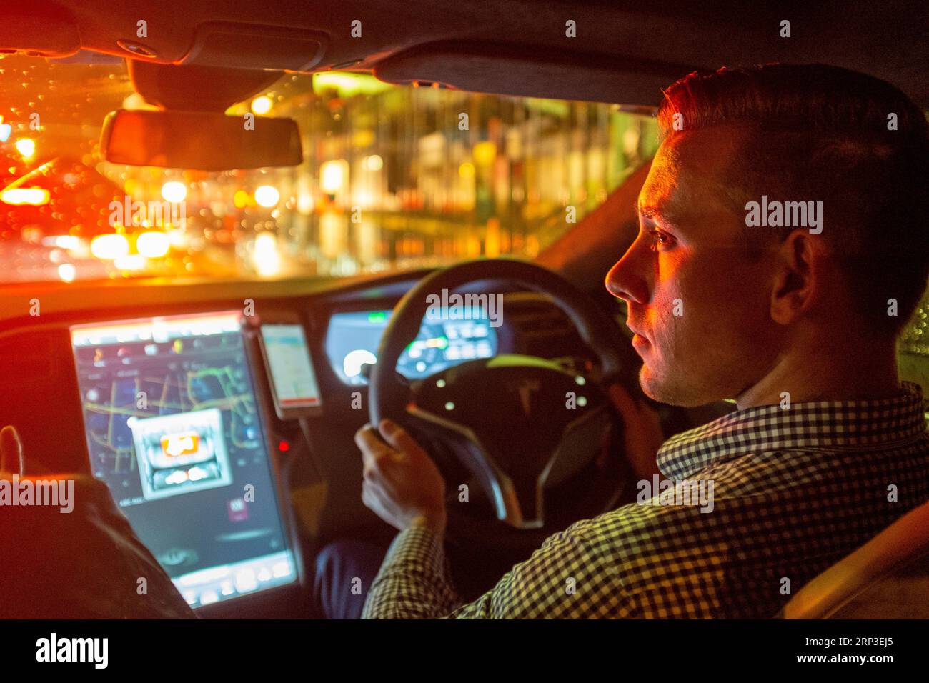 Guida Uber al volante di un veicolo elettrico Tesla di notte sotto la pioggia Foto Stock