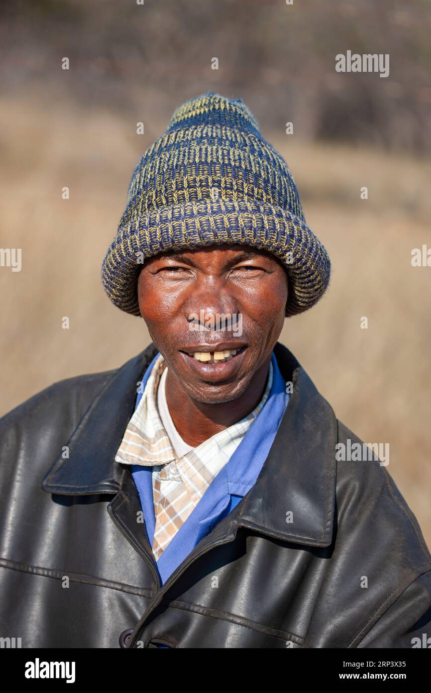 villaggio africano con berretto e giacca di pelle, ritratto all'aperto nel cortile della sua casa Foto Stock