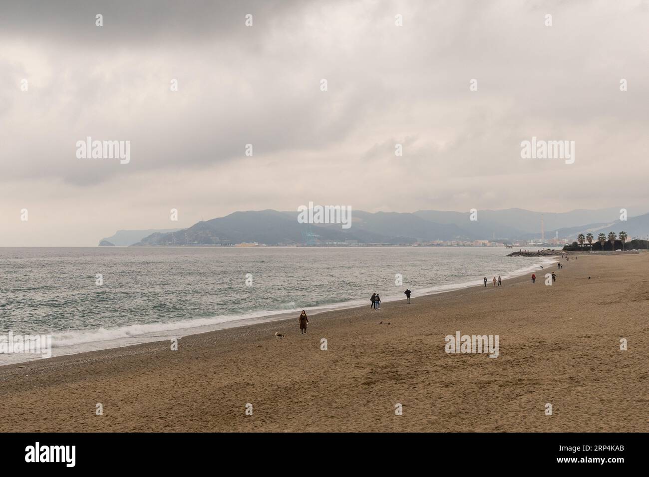 Vista sopraelevata della spiaggia in bassa stagione con persone che camminano sulla riva e sulla costa sullo sfondo in una nuvolosa giornata invernale, Savona, Liguria Foto Stock