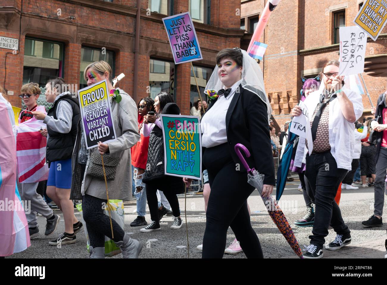 Sfilata del Manchester Pride 2023. REGNO UNITO. Donna in completo con papillon. Testo del cartello Ban Conversion Therapy Theme Queerly Loved. Foto Stock