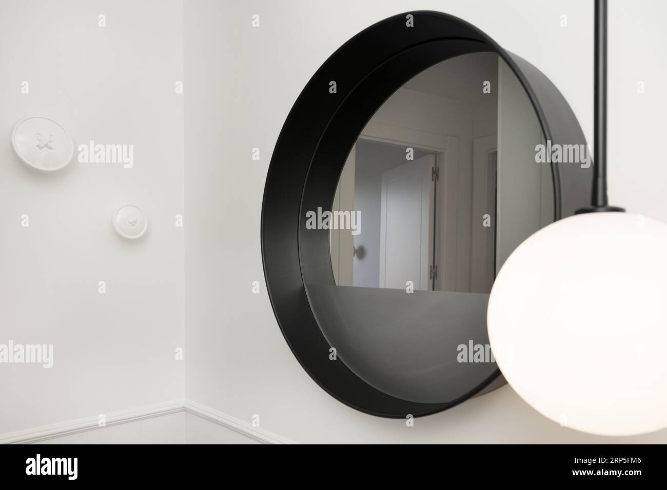 Specchio circolare decorativo con cornice nera profonda accanto a un paralume a globo Foto Stock