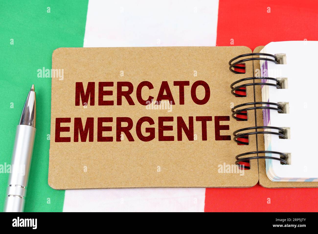 Economia e finanza. Sulla bandiera italiana si trova una penna e un taccuino con l'iscrizione - mercato emergente. Testo in italiano. Foto Stock