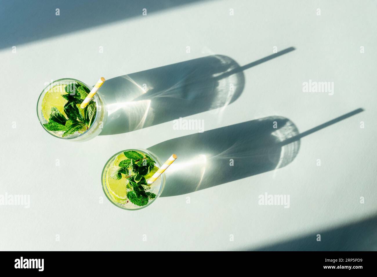 Due bevande mojito con cannucce sul tavolo blu. Bevande rinfrescanti fredde. Ombre lunghe e dure. Vista dall'alto, base piatta. Foto Stock