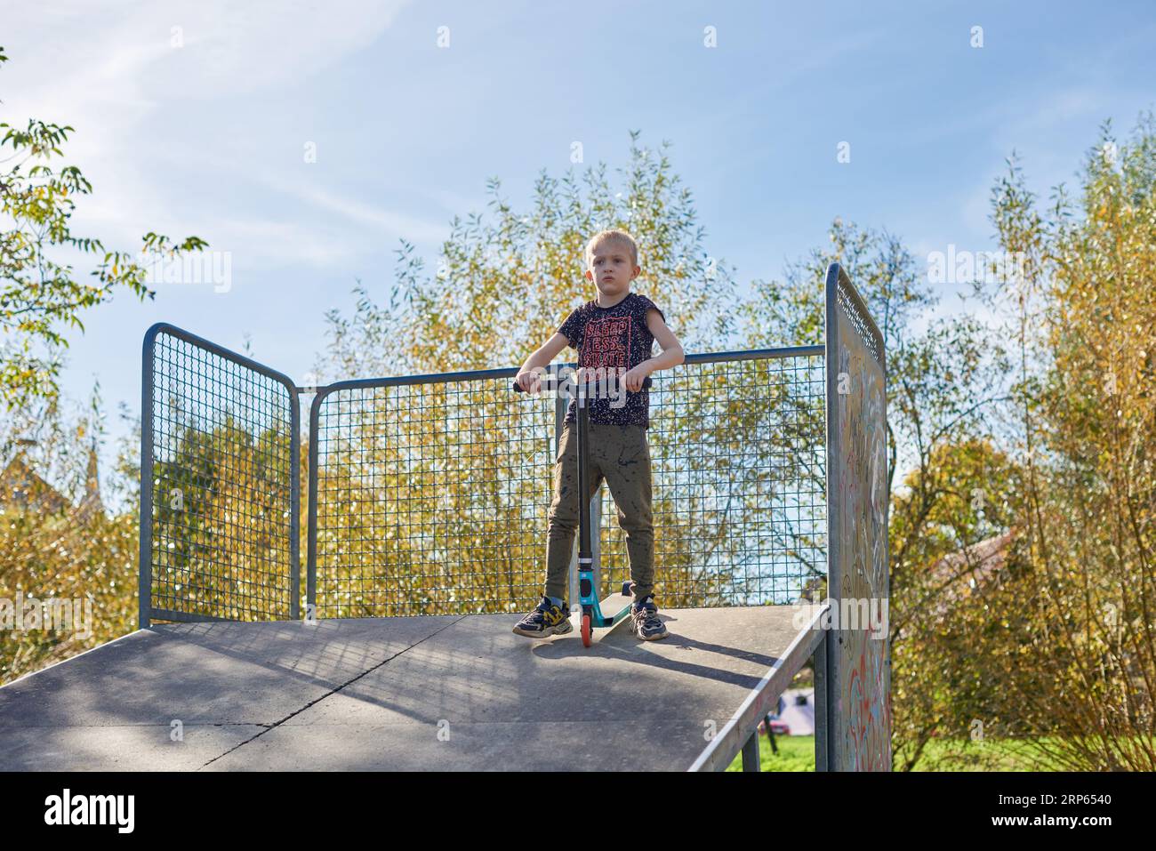 Il ragazzo in scooter fa un trucco e si diverte a correre nello skate Park durante la nuvolosa giornata primaverile. Un giovane che fa un trucco sullo scooter nel parco. Fu Foto Stock