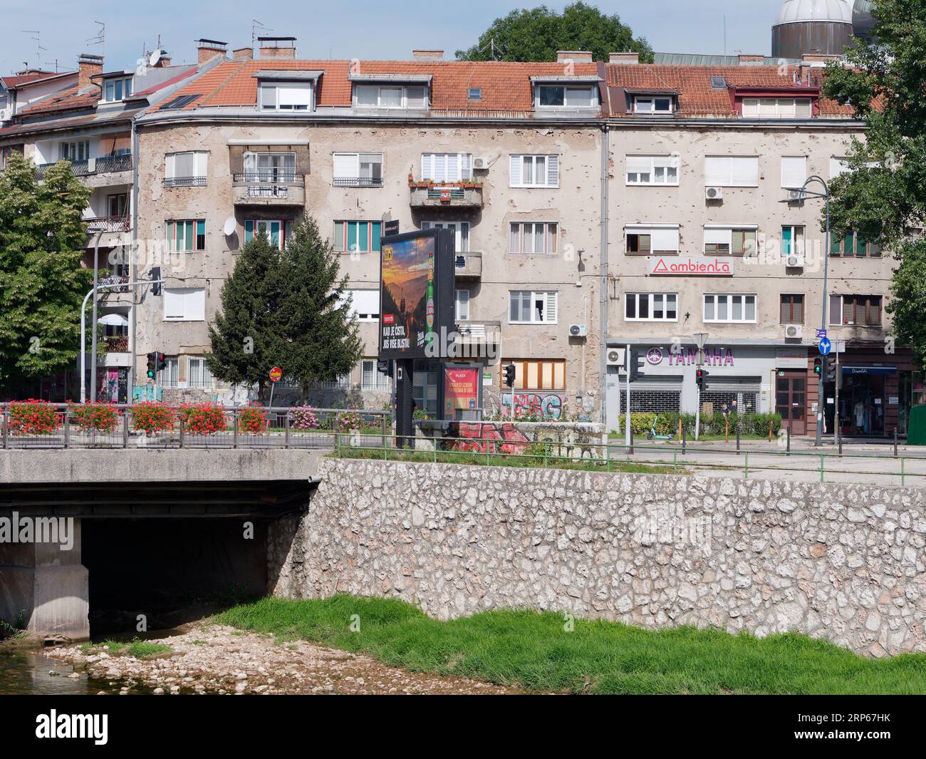 Appartamento a più piani con fori per proiettili e negozi al piano terra vicino al fiume Miljacka a Sarajevo, Bosnia ed Erzegovina, 3 settembre 2023 Foto Stock