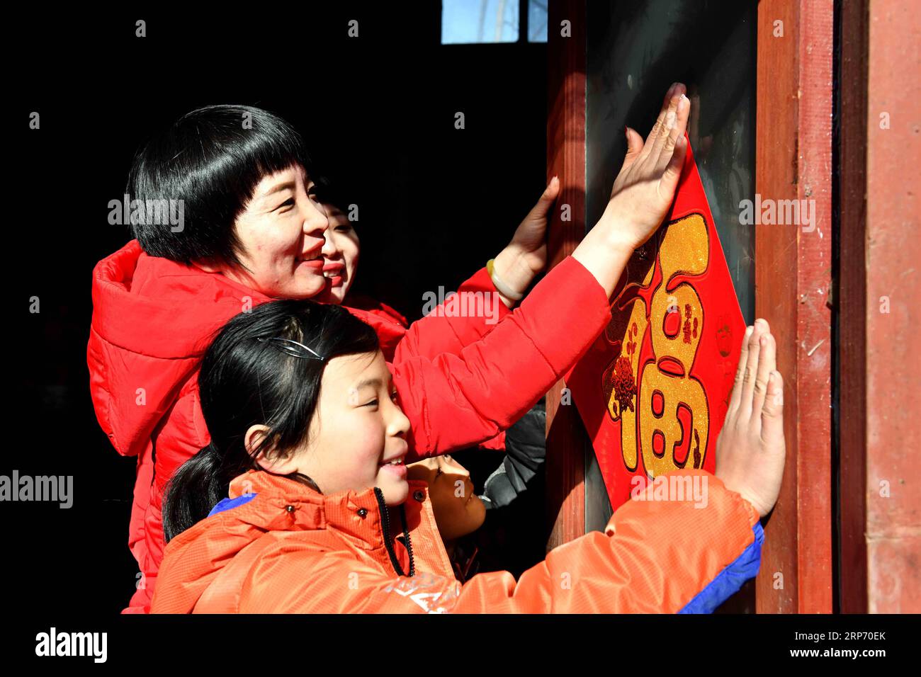 (190123) - JINAN, 23 gennaio 2019 (Xinhua) -- volontario GU Shengyuan incolla un poster del personaggio cinese fu , che significa buona fortuna, su una porta con Nuonuo (davanti) nel villaggio di Wucun della città di Linyi, nella provincia di Shandong della Cina orientale, 16 gennaio 2019. Le sorelle gemelle GU Shengyuan e GU Shengyan sono membri di un gruppo di servizio volontario che aiuta i bambini orfani e impoveriti che vivono nelle aree montane di Linyi. Fondato il 19 aprile 2018, il gruppo con oltre 6.000 volontari fornisce supporto a più di 3.500 bambini orfani e impoveriti. (Xinhua/Guo Xulei) CHINA-SHANDONG-ORPHANED CHILDR Foto Stock