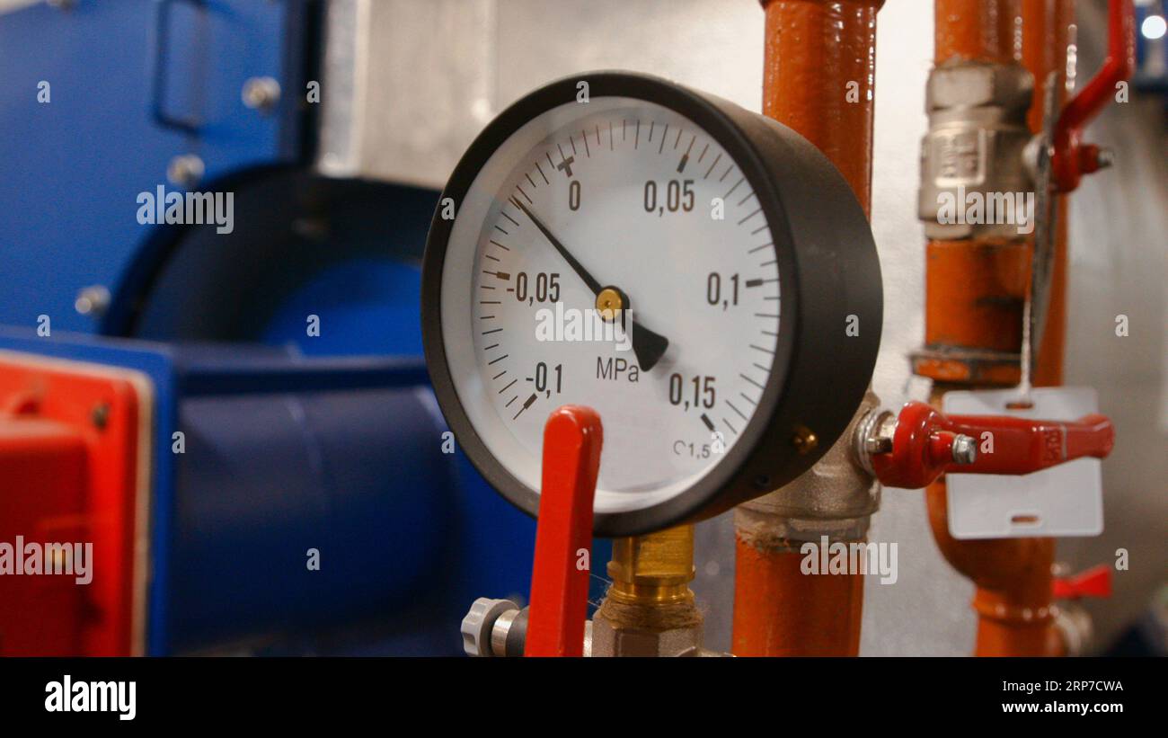 Il manometro con una freccia e numeri mostra la pressione dell'acqua nei tubi nella sala caldaia Foto Stock