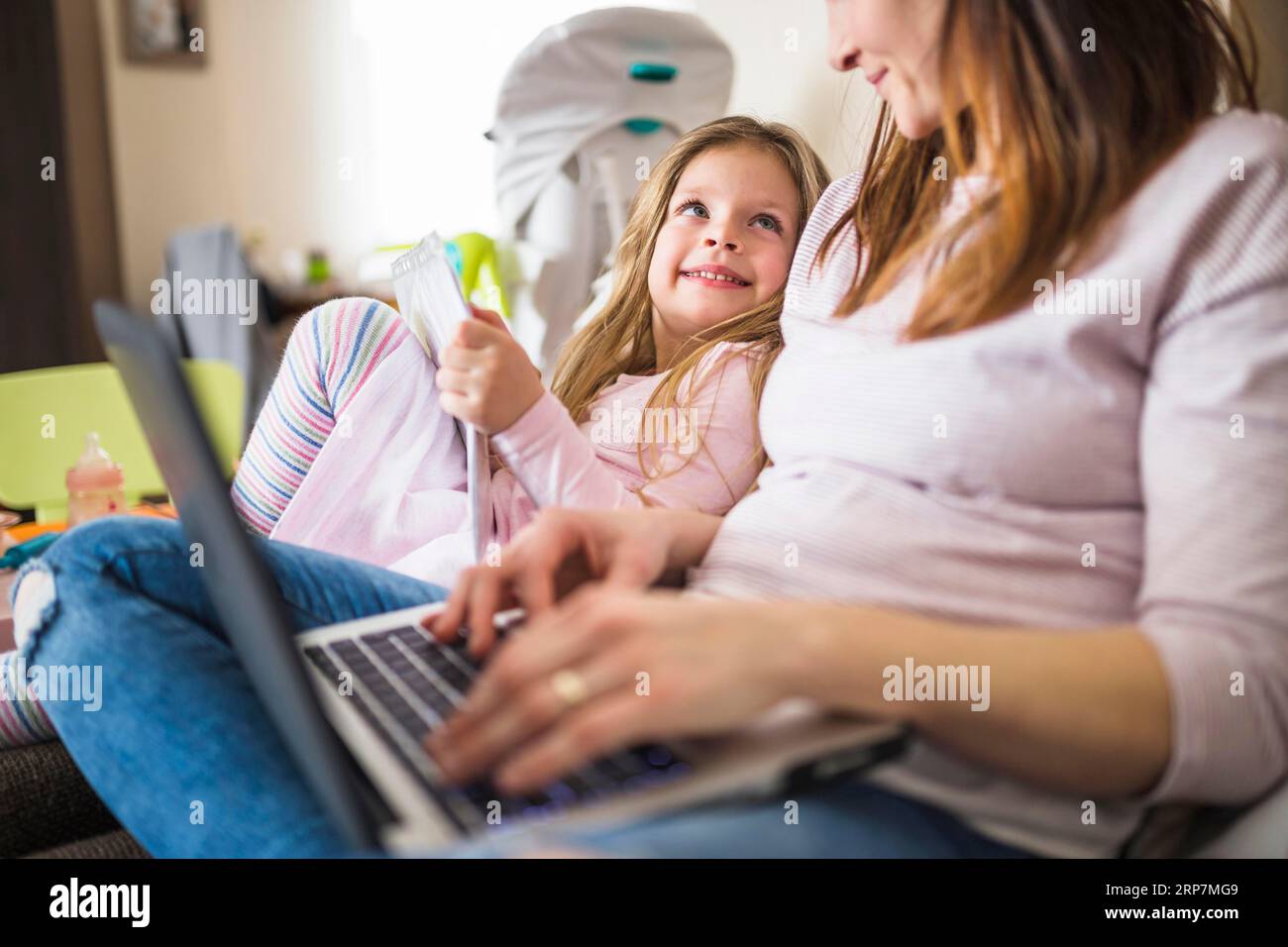 Ragazza sorridente carina che guarda la madre usando un computer portatile Foto Stock