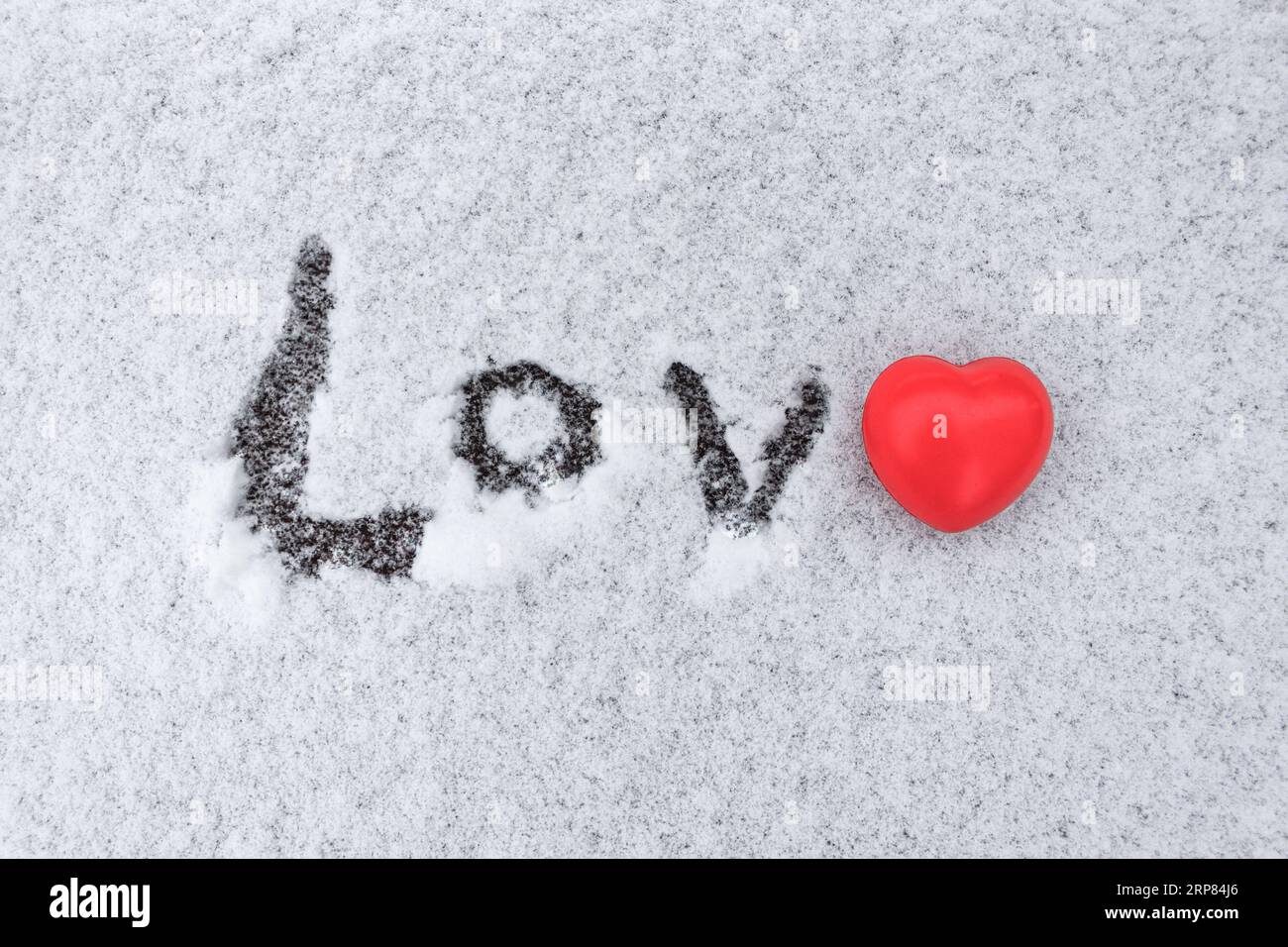La parola amore scritta nella neve con una statuetta a cuore rosso invece della lettera e Foto Stock