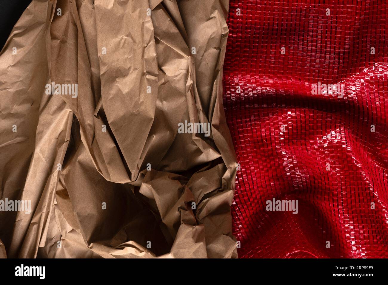 Primo piano di carta da imballaggio marrone stropicciata e di una rete di plastica tessuta rossa per il confezionamento di prodotti alimentari. Sfondo primo piano astratto. Foto Stock