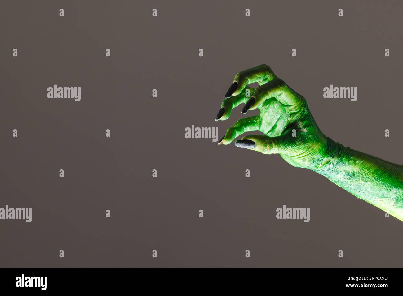 Mano mostro verde con unghie nere che raggiungono lo sfondo grigio Foto Stock