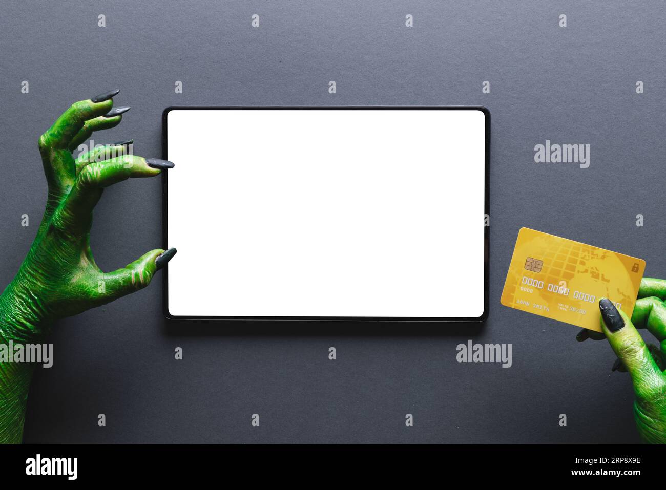 Lancette di mostri verdi che tengono la carta di credito e il tablet con spazio per la copia su sfondo grigio Foto Stock