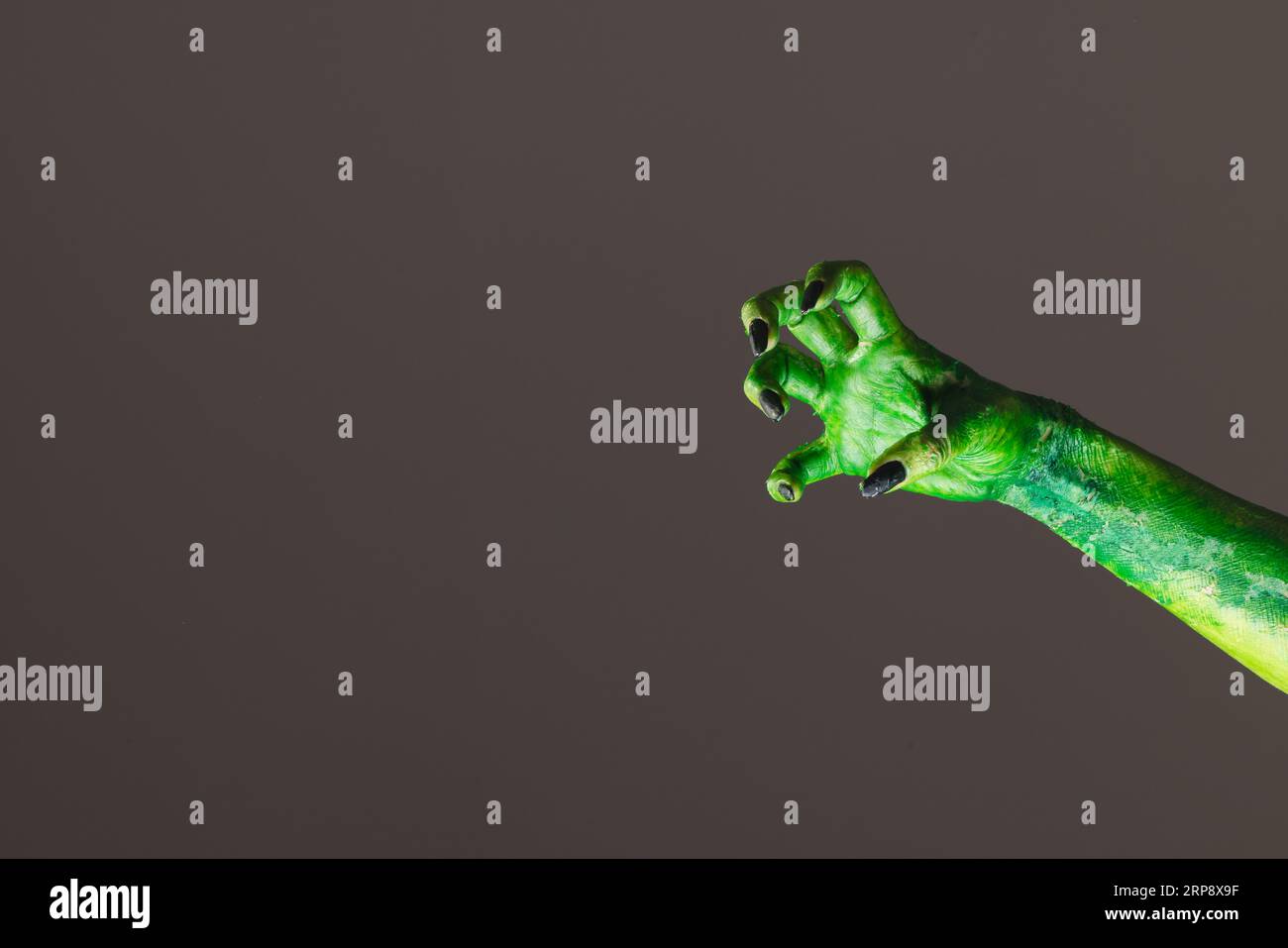 Mano mostro verde con unghie nere che raggiungono lo sfondo grigio Foto Stock