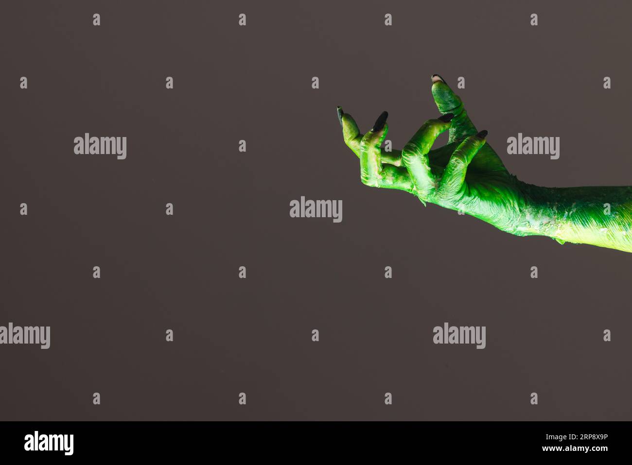 Mano mostro verde con unghie nere che raggiungono lo sfondo grigio Foto Stock