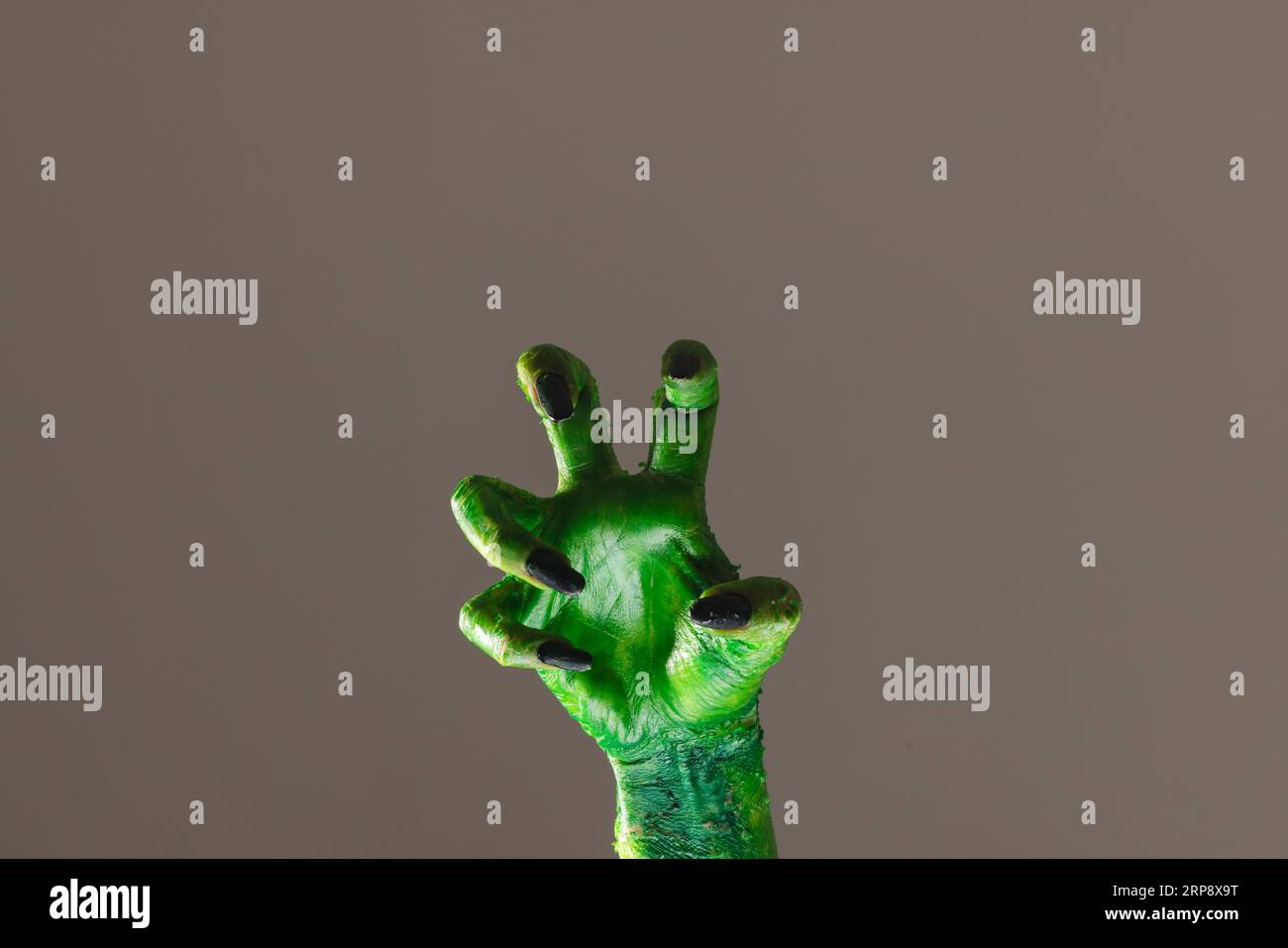 Mano mostro verde con unghie nere che raggiungono lo sfondo grigio Foto Stock