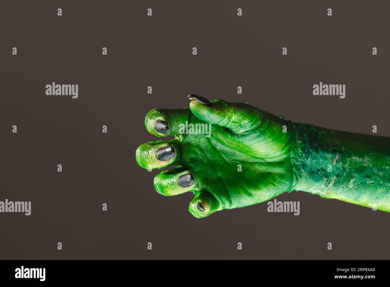 Mano mostro verde con unghie nere che raggiungono lo sfondo grigio Foto Stock