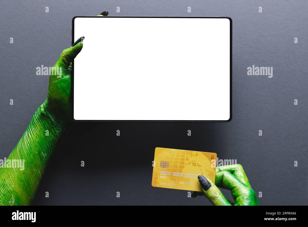 Lancette di mostri verdi che tengono la carta di credito e il tablet con spazio per la copia su sfondo grigio Foto Stock