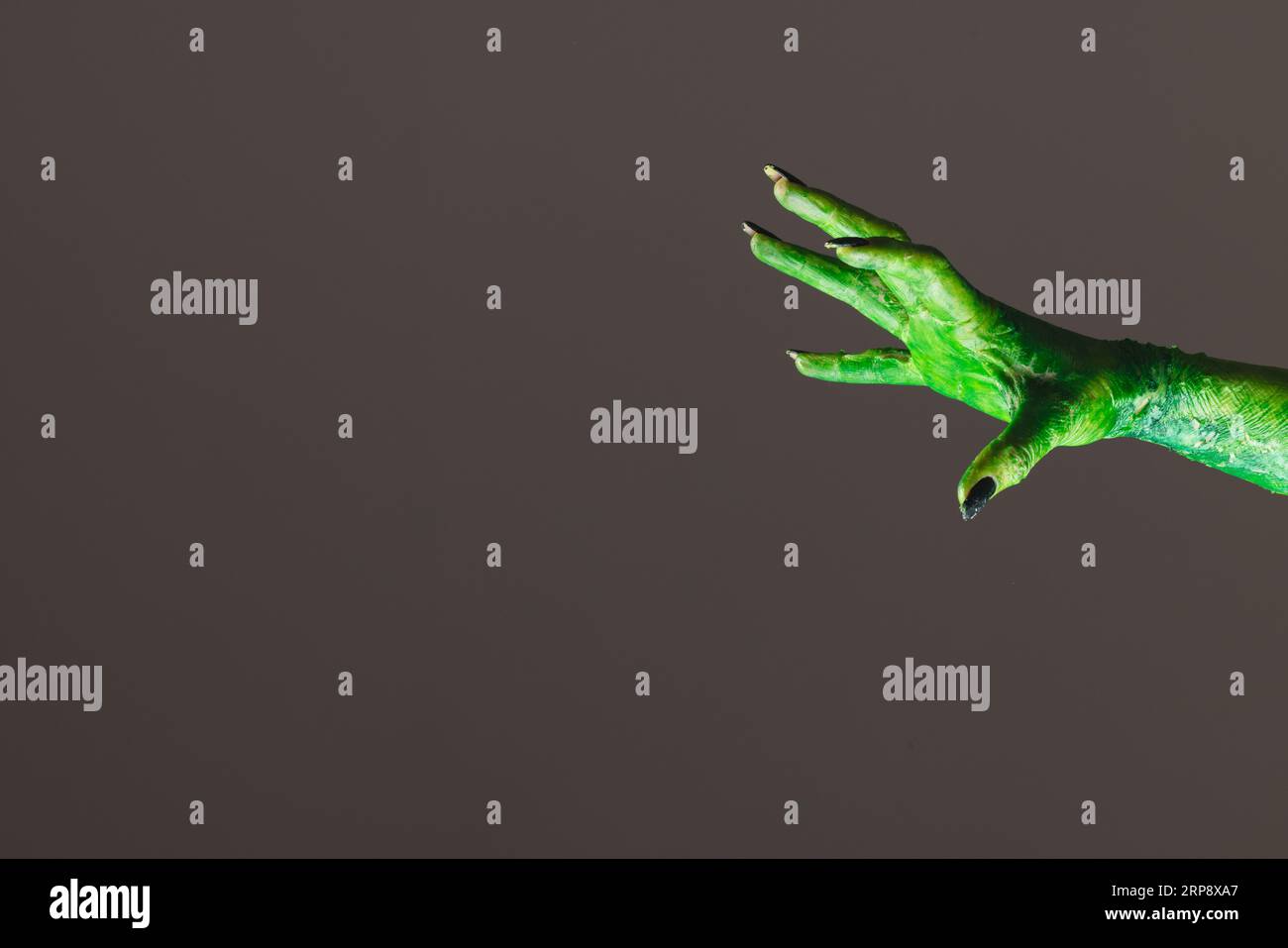 Mano mostro verde con unghie nere che raggiungono lo sfondo grigio Foto Stock