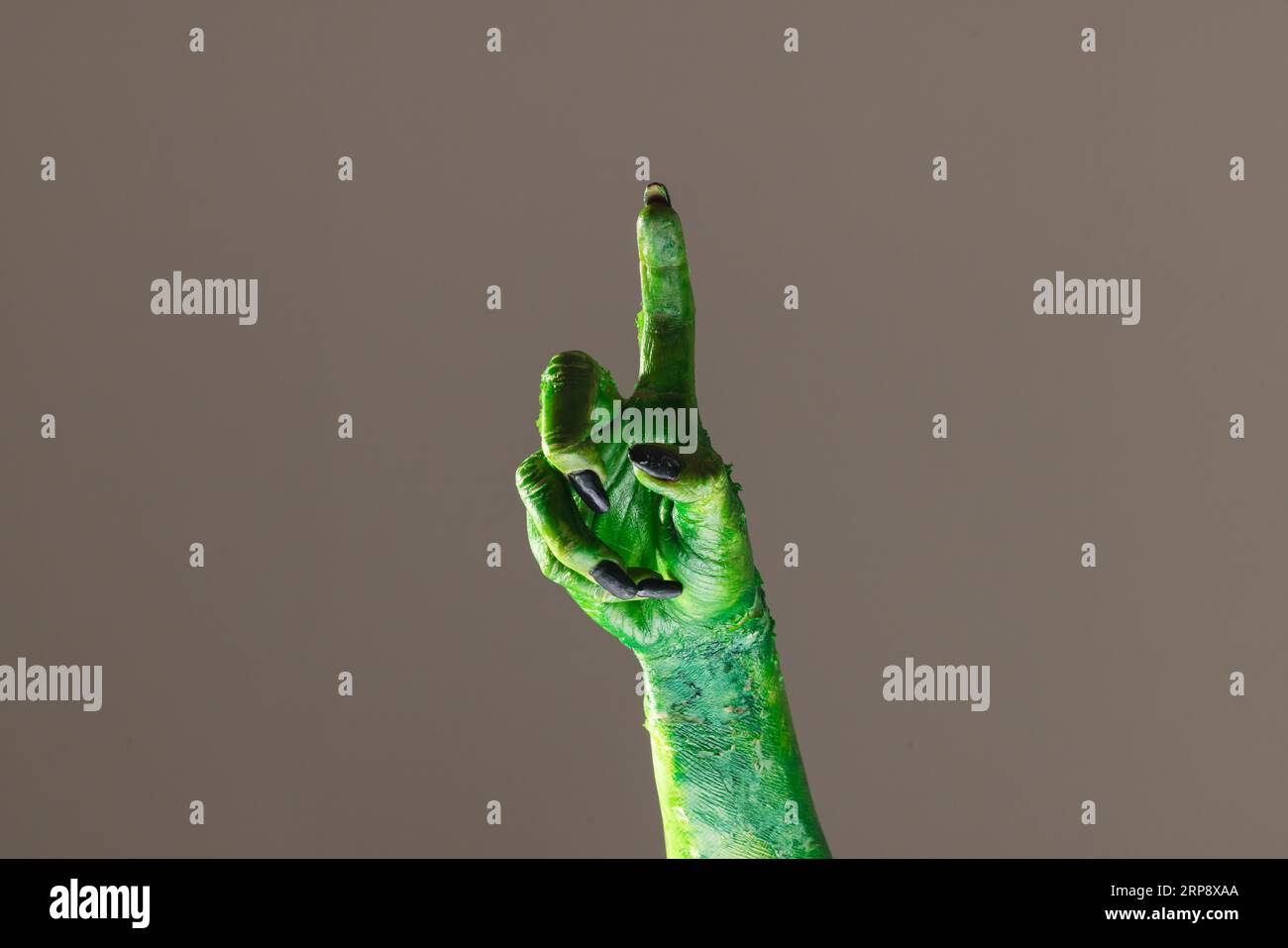 Mano mostro verde con unghie nere che puntano con il dito su sfondo grigio Foto Stock