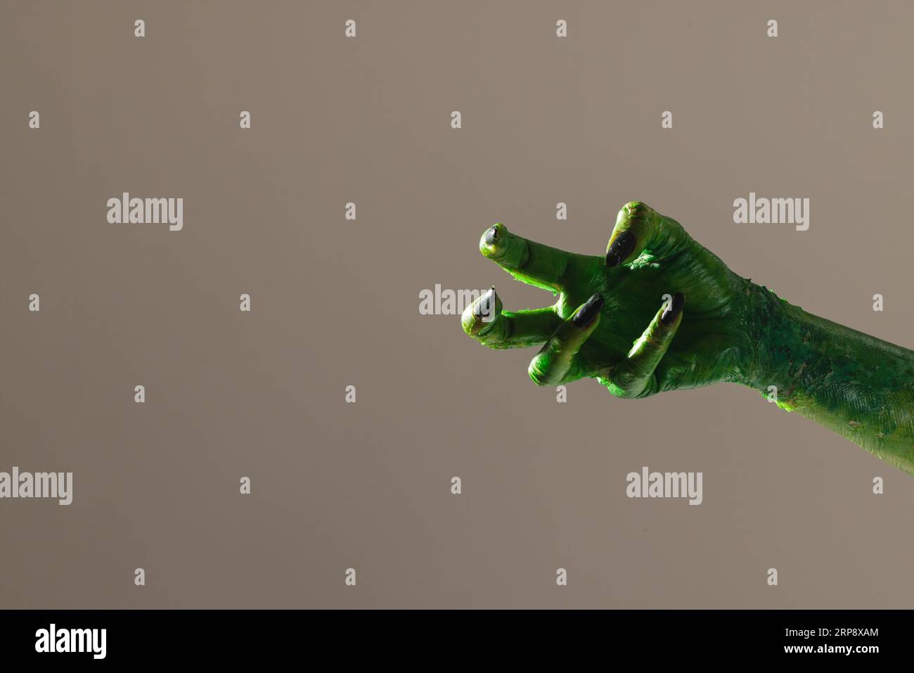 Mano mostro verde con unghie nere che fanno gesto su sfondo grigio Foto Stock