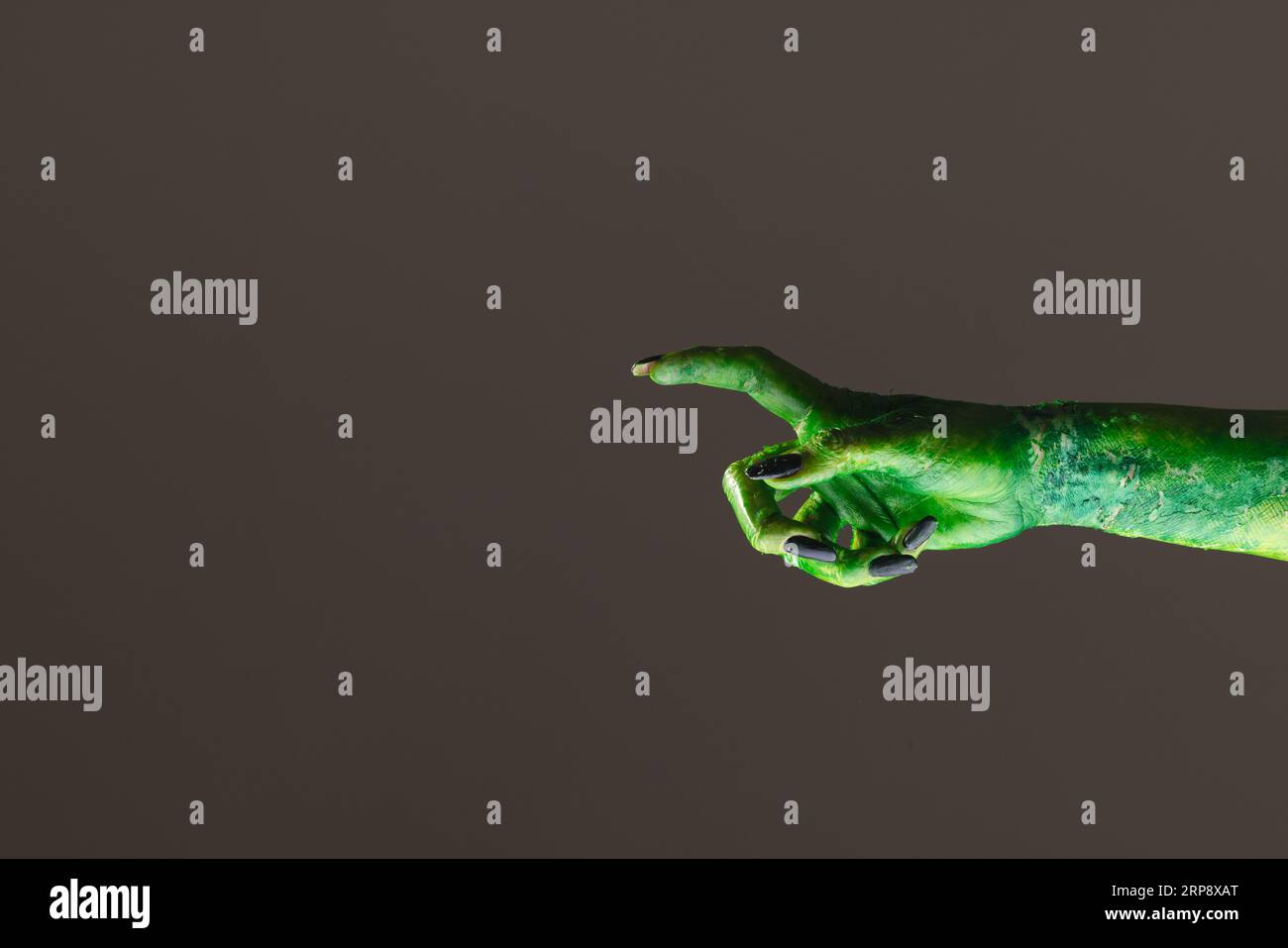 Mano mostro verde con unghie nere che puntano con il dito su sfondo grigio Foto Stock